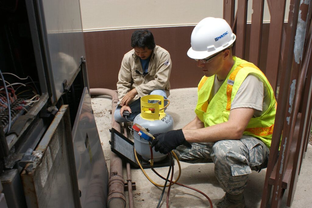 HVAC manager resume examples should reflect your hands-on expertise in the field, as seen in this photo of an HVAC manager working and assisted by another employee 