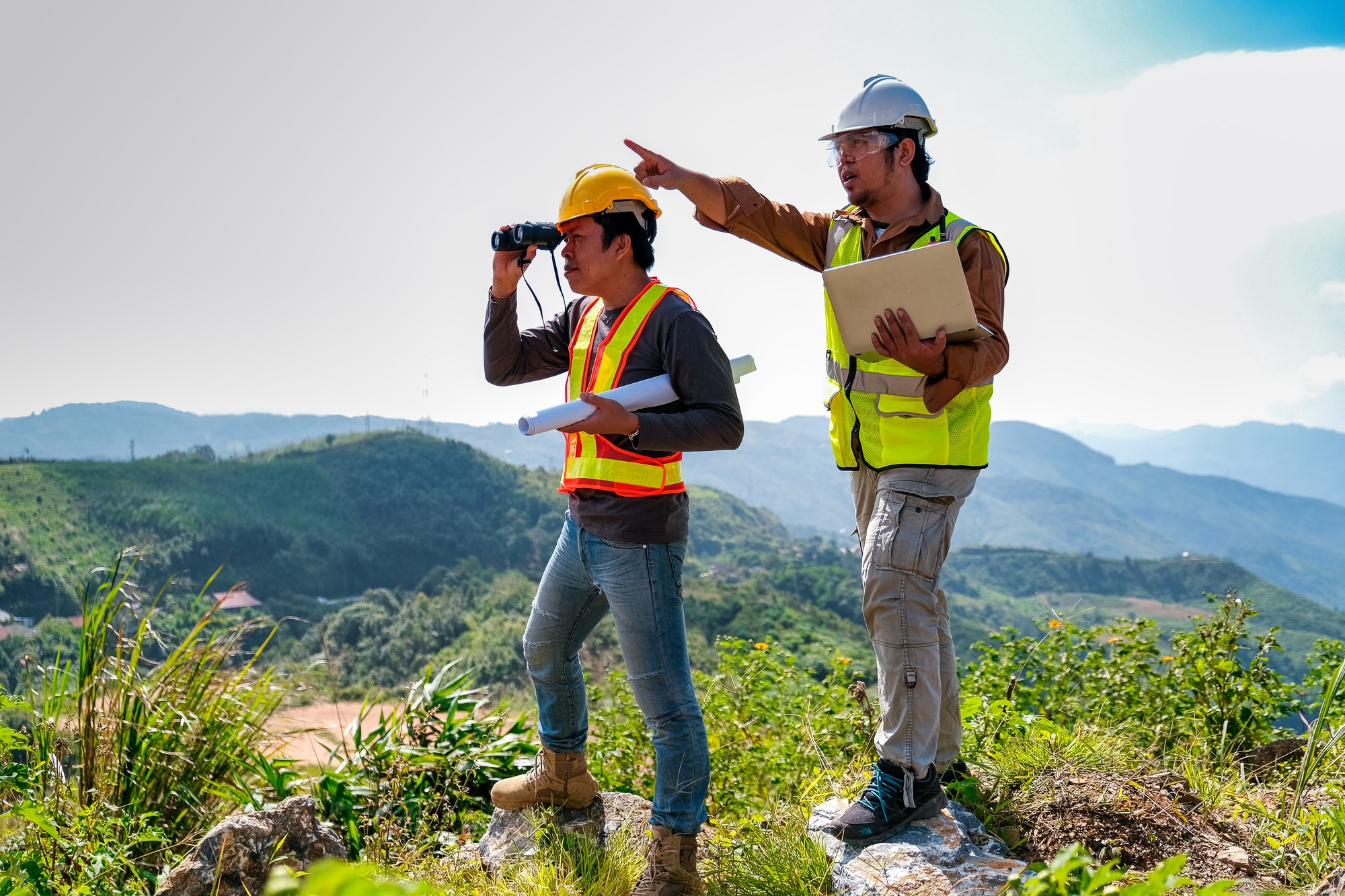 Engineer man with laptop point to forward direction while his team use binoculars look to their work