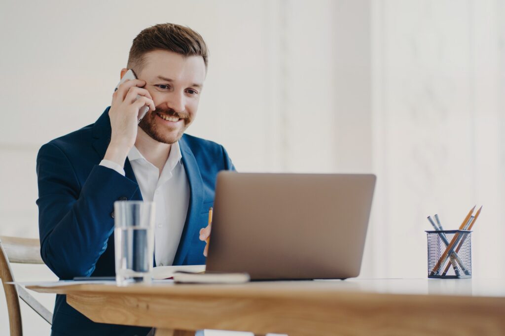 Young stylish executive talking on phone in front of laptop behind office desk