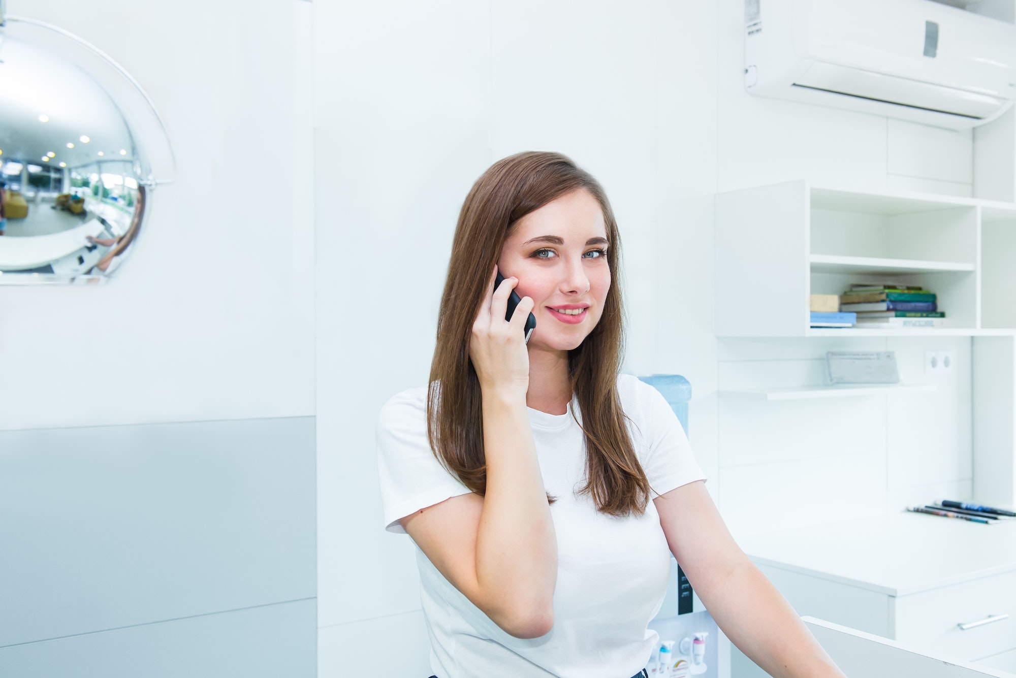 Young woman administrative manager talking on phone sitting behind the reception desk.